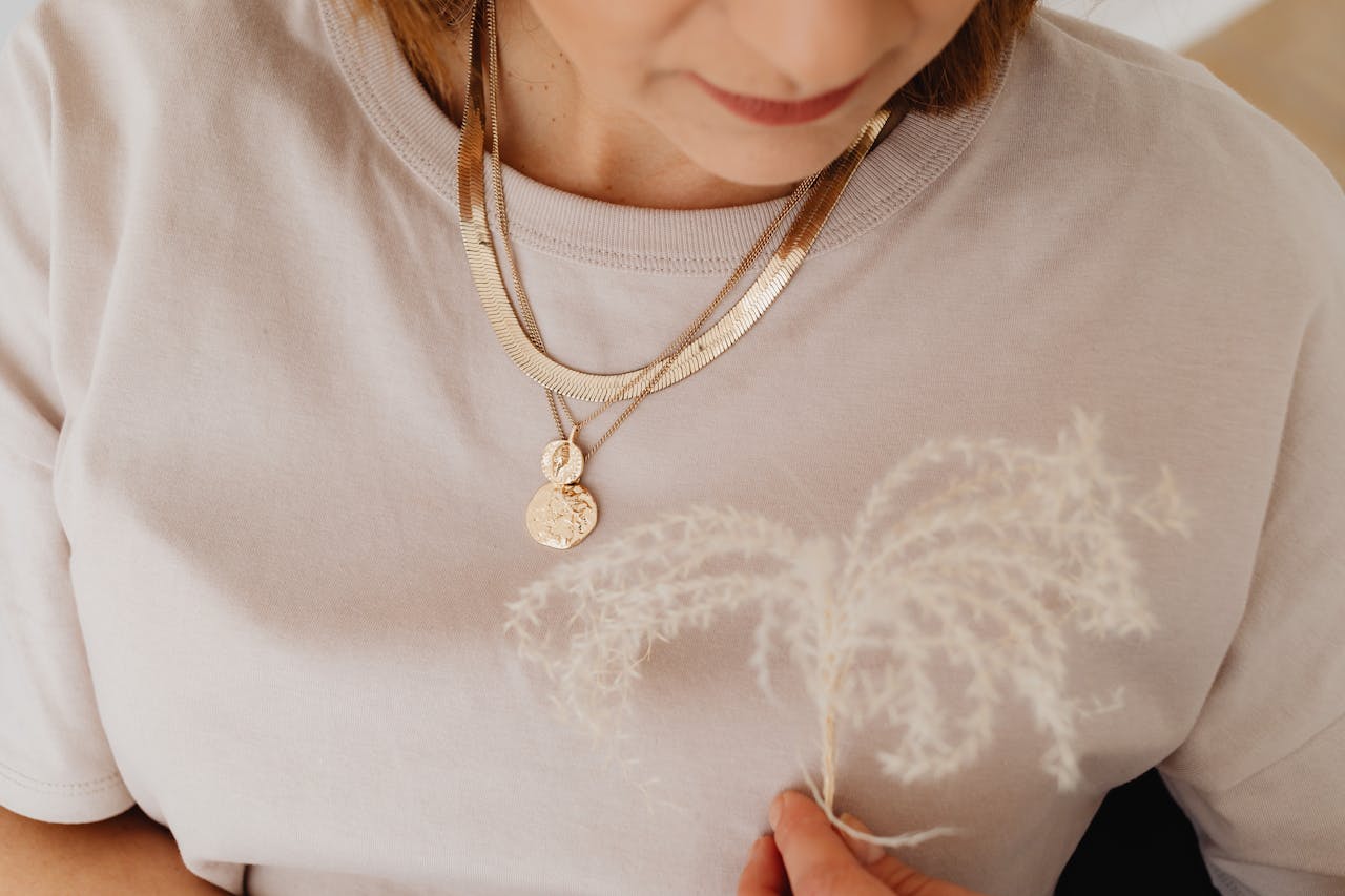 Close-up of a woman wearing gold necklaces and holding pampas grass, showcasing elegance and style.